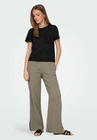 Svart t-shirt med korta ärmar och en strukturerad fickdesign, tillsammans med vida, ljusbruna byxor med subtila sprund vid fållen.