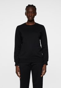 Svart sweatshirt med rund hals, långa ärmar och ribbade manschetter. Tillverkad av texturerat tyg, med en subtil logotyp på bröstet.