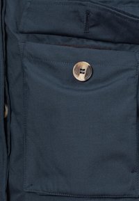 Material de jachetă bleumarin cu un buzunar frontal dotat cu închidere prin buton metallic. Textură netedă și linii curate, care evidențiază funcționalitatea.