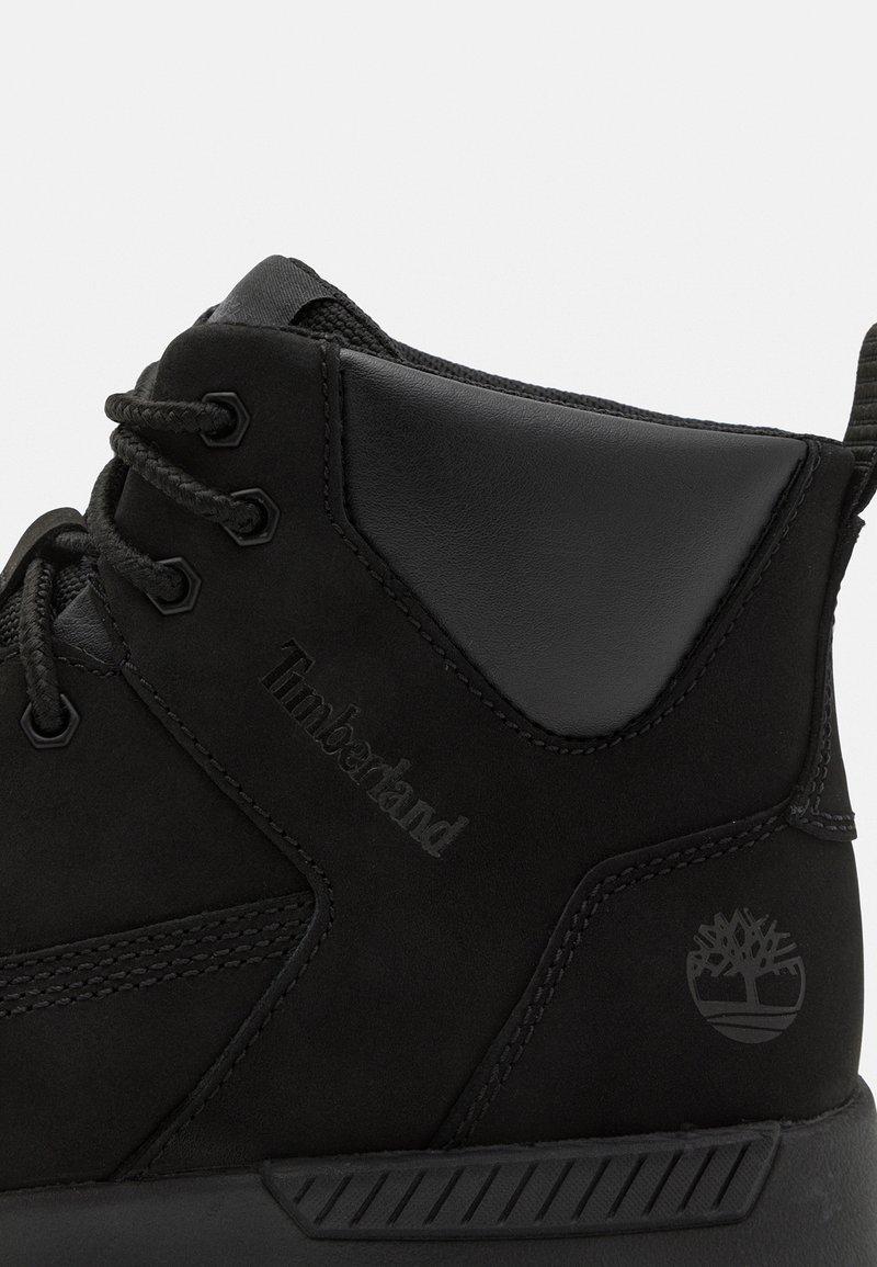 Schwarze Wildleder-Ankle-Boots mit einer glatten Lederakzent, robusten Schnürsenkeln, geprägtem Logo und einem Markenemblem an der Ferse.