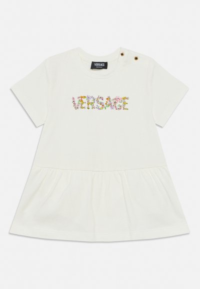 Λευκό φόρεμα με κοντά μανίκια και βολάν στο τελείωμα, με λουλουδάτο λογότυπο "Versace" στο στήθος και δύο διακοσμητικά χρυσά κουμπιά στον αριστερό ώμο.