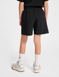 Svarta, lätta shorts med resårmidja, som bärs med vita ankelsockor och grå sneakers med gummisula.