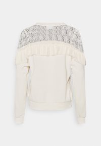 Krémový top s dlouhým rukávem, krajkovým živůtkem a volánkovým lemem na horní části zad, žebrovanými manžetami a spodním lemem.