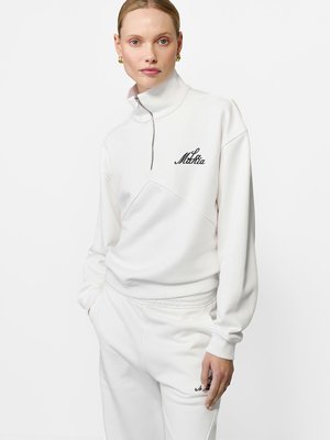 Hanorac alb cu fermoar, cu guler înalt și logo negru brodat. Prezintă un design pe panouri și pantaloni sport albi asortați. Textură de material moale.