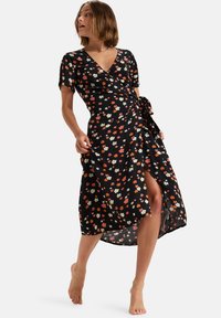 Robe noire à manches courtes avec un motif floral rouge, jaune et blanc. Elle possède une taille cintrée à nouer et une fente sur le devant pour plus de liberté de mouvement.