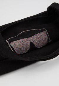 Black canvas bag featuring a multicolored, pixelated sunglasses graphic inside. Smooth texture with a zip closure.