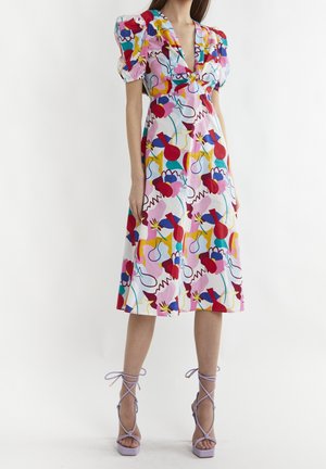 Frau trägt ein buntes abstraktes florales Midikleid mit Puffärmeln und lavendelfarbenen Schnürhighheel-Sandalen.