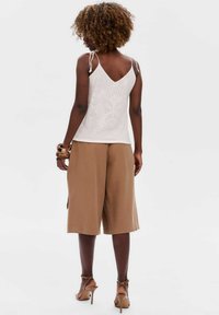 Witte, gebreide camisole met verstelbare bandjes, met een v-hals en een patroonstructuur. Gecombineerd met bruine, loszittende culottes.