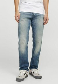 Vaqueros de mezclilla azul deslavado con corte recto, presentan un sutil desgaste, cinco bolsillos y un lavado medio. Combinados con zapatillas grises.
