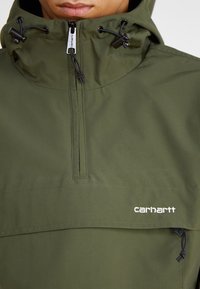 Grüne Kapuzenjacke mit einem Halb-Reißverschluss-Design, verstellbaren Kordeln und einer Fronttasche. Mit Carhartt-Logo in Weiß.