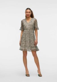 Vestido corto y transparente con un patrón de cebra en beige y negro, con escote en V, mangas acampanadas y un dobladillo con volantes. Combinado con sandalias de tacón verdes.