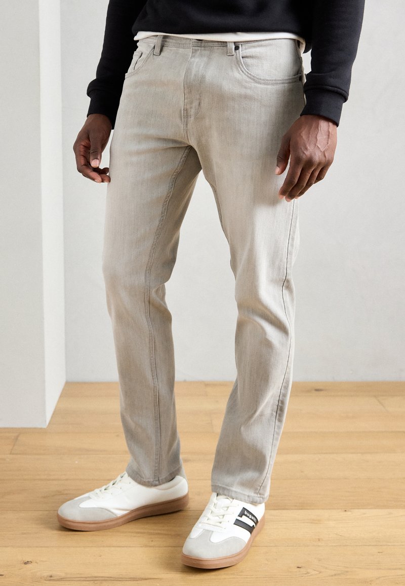 Lys grå denimjeans med slim fit, der har subtil slidtage, frontlommer og bæltestropper. Bæres med hvide sneakers.