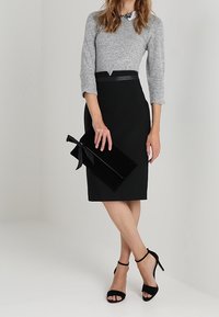 Grå stickad tröja, svart blyertskjol med midjebälte, svart kuvertväska med rosettdetalj och svarta remsandaler. Släta och texturerade ytor.