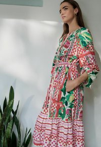 Rochie colorată cu un model floral și geometric, având mâneci lungi, o curea la talie și o fustă în straturi. Țesătură din bumbac.