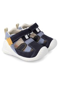 Zapatos de tela azul y marino con correas de velcro, suelas de goma blanca y paneles de malla para transpirabilidad, con acentos de costura amarilla.