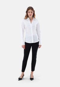 Camicia bianca a maniche lunghe con colletto e chiusura con bottoni, abbinata a pantaloni neri slim-fit e tacchi a punta neri.