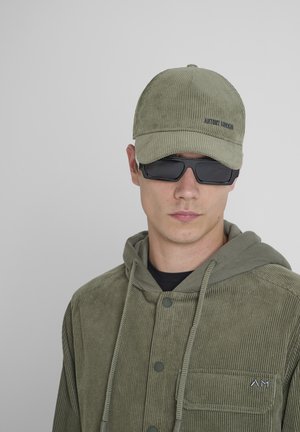 Gorra de canalé verde oliva con un acabado texturizado, combinada con una chaqueta de canalé a juego que presenta una capucha y detalles de botones.