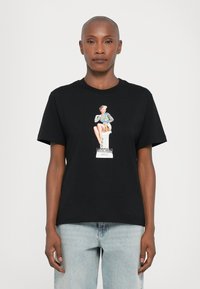 Juodas medvilnės marškinėliai su centriniu grafinio vaizdu, vaizduojančiu sėdintį personažą spalvingais drabužiais, su užrašu "MOSCHINO JEANS" apačioje. Trumpomis rankovėmis.