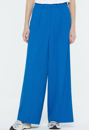 Royal blue wide-leg trousers made of smooth fabric, featuring a front pleat and a button closure at the waist. Worn with gray athletic shoes.