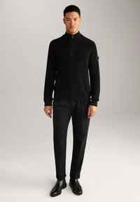 Schwarzer gerippter Strick-Half-Zip-Pullover mit hohem Kragen, kombiniert mit taillierten schwarzen Hosen und schwarzen Leder-Stiefeletten.