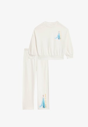 Zestaw białej bluzy i spodni z krótszym, skróconym krojem. Bluza ma grafikę postaci oraz tekst na nogawce.