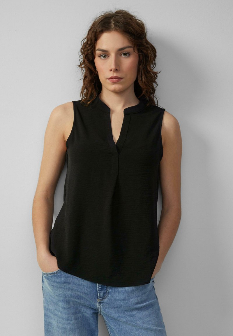 Zwarte mouwloze top met een kraag en een V-halslijn, die een losse pasvorm en een lichte textuur heeft. Gecombineerd met blauwe jeans.