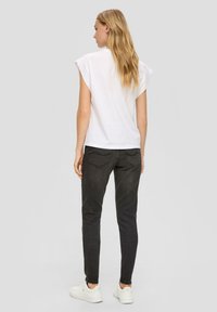 Witte top met korte mouwen en een relaxte pasvorm, gecombineerd met strakke zwarte jeans en witte sneakers. Eenvoudig ontwerp, zonder zichtbare patronen of accenten.