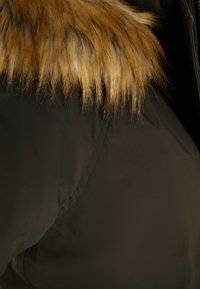 Sort overtøj med en blød tan faux fur krave, der har en glat stoftekstur og en skjult lynlåse-design.