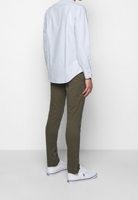 Ljusblå randig skjorta med knappar, olivgröna byxor och vita sneakers. Skjortan har en rundad fåll; byxorna är slim fit.