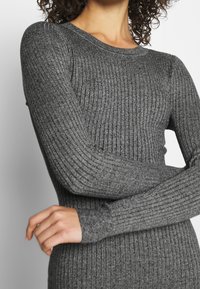 Abito a maglia grigio a maniche lunghe con coste, caratterizzato da un collo rotondo e una silhouette aderente. Texture morbida con lieve elasticità e design lineare.