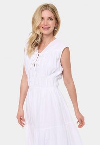 Rochie albă din bumbac, cu talie strânsă, mâneci scurte și broderie din dantelă. Prezintă un decolteu în V și un detaliu cu fundiță la gât.