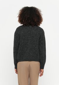 Suéter de malha cinza-escuro com gola redonda, textura canelada e ajuste ligeiramente solto, usado sobre calças bege.