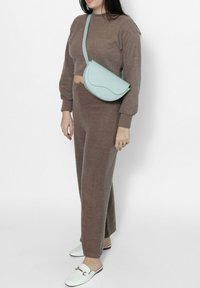 Completo in maglia marrone a due pezzi con maniche lunghe e pantaloni a gamba larga, abbinato a una borsa a tracolla azzurro chiaro e scarpe slip-on bianche.