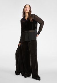 Czarna aksamitna bluzka z prześwitującymi rękawami i zapinana na guziki z przodu. W zestawie z czarnymi aksamitnymi spodniami z wysokim stanem, szerokimi nogawkami i spiczastymi obcasami.