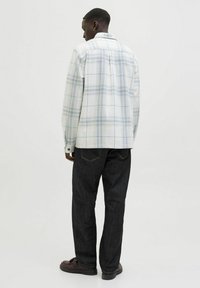 Witte geruite shirt met lichtblauwe lijnen, met knoopsluiting kraag en rugpas; gecombineerd met donkerdenim broek en bruine schoenen.