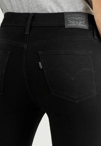 Vaqueros de mezclilla negra con una cintura de altura media, que cuentan con dos bolsillos traseros, detalles de costura sutiles y un parche con el logo de Levi Strauss & Co.