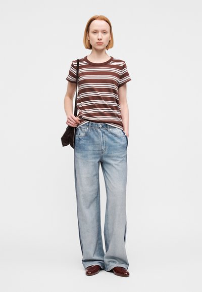 Καφέ και λευκό ριγέ μπλουζάκι, άνετο τζιν παντελόνι ανοιχτού μπλε χρώματος και καφέ παπούτσια. Συμπληρώνεται με μία σκουρόχρωμη τσάντα ώμου. Απλός σχεδιασμός.