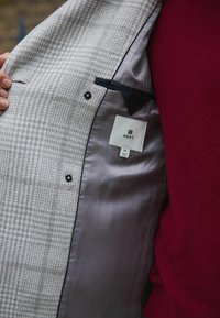 Harmaan houndstooth-kuosiset bleiserin sisäosat mustalla läpällä, kaksinappisuljenta ja lappu; sileä tummanharmaa satiinivuori.