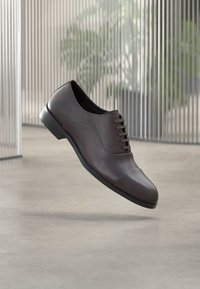 Barna bőrből készült elegáns cipő sima felülettel, lekerekített orral és öt fűzőlyukkal. Kontrasztos orrkaptár díszítéssel.