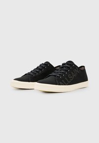 Sneakers neri in tela con suole in gomma bianca, dotate di lacci scuri e un grande logo nero "ALLSAINTS" sul lato. Design a profilo basso.