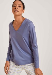 Paarse long-sleeve top met een V-hals ontwerp. Gladde textuur. Gecombineerd met pantalon met een patroon van geometrische vormen in geel en blauw.
