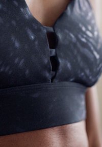 Črn športni bralette z gladkim teksturnim materialom, izrezom spredaj in širokim podpornim trakovi na dnu.