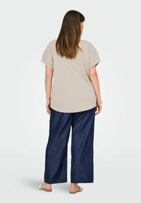 Beige oversized skjorte med optrækkede ærmer, parret med loose-fit marineblå denim bukser og lyse sandaler. Enkel design, struktureret stof.
