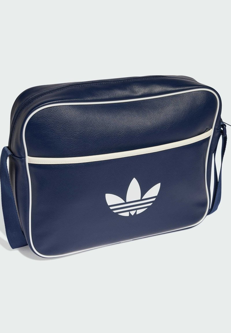 Navyblå taske i syntetisk materiale med hvide kanter og et stort hvidt trefoil-logo foran. Har en skulderrem og lynlåslukning.