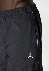 Svart idrettsshorts laget av lett, teksturert stoff. Har en elastisk midje og en hvit Jordan-logo på venstre side.