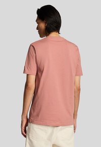 Camiseta de manga corta de algodón en color rosa empolvado, diseño de cuello redondo con una textura suave, vista desde atrás con detalles de costura visibles.
