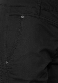 Černé kalhoty s hladkým, texturovaným materiálem a detailním pohledem na švy a stříbrný knoflík na kapse.