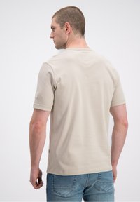 Beżowy t-shirt z krótkim rękawem i zaokrąglonym dekoltem, z subtelnym szwem z tyłu, wykonany z gładkiej tkaniny, zestawiony z jasnoniebieskimi jeansami.