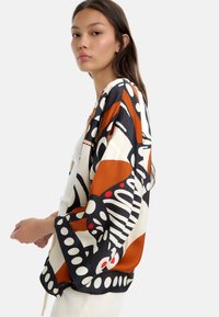 Top w stylu kimono z odważnym abstrakcyjnym wzorem w odcieniach pomarańczowym, czarnym i białym, z szerokimi rękawami i luźnym krojem. Gładka faktura tkaniny.