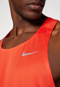 Camiseta sin mangas para hombre en tejido rojo brillante con una textura transpirable, que presenta un pequeño logo plateado de Nike en el pecho.